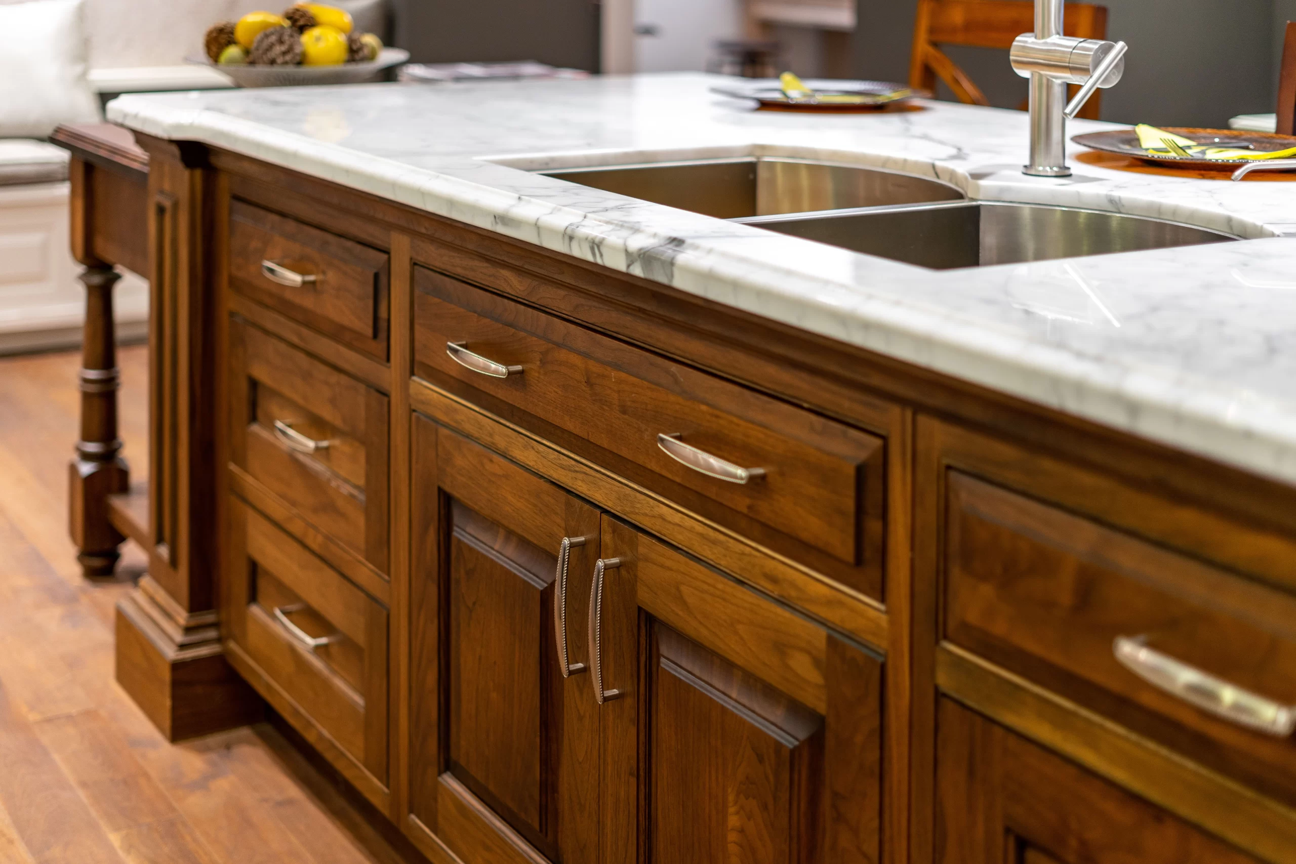 Luxury kitchen island featuring rich wood cabinetry, a marble countertop, and a stainless steel double-basin sink with a modern faucet.